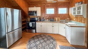 A compact kitchen with wooden walls, a stainless steel refrigerator, a microwave, a stove, and a sink. - Sea Esta: Perfect Getaway on the Canal with Boat Dock (Ocracoke)