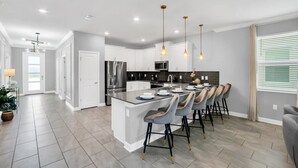 Une cuisine moderne avec des meubles blancs, des appareils en acier inoxydable et un îlot central doté de tabourets de bar.