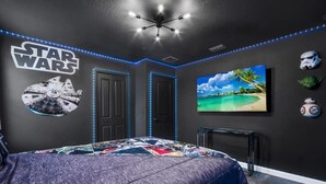 Une chambre décorée sur le thème de Star Wars, avec un grand lit, des œuvres d’art murales de Star Wars, un tableau représentant une plage et des casques de Star Wars accrochés au mur.