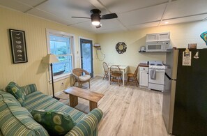 A compact living space with a sofa, dining table, chairs, a kitchenette, and a ceiling fan. - Sea-Esta Downstairs: On the Canal with Boat Dock (Ocracoke)