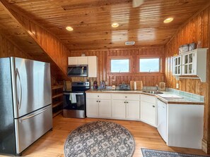 A compact kitchen with wooden walls, a stainless steel refrigerator, a microwave, a stove, and a sink. - Sea-Esta Upstairs: A Couple's Getaway on the Canal (Ocracoke)