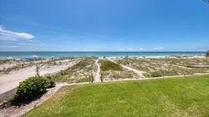 A beach view with a clear sky, sandy paths, and a grassy area. - Gorgeous Panoramic Views!  Stairs DIRECTLY to the beach!  PELICANS POINTE 5C (Indian Shores)