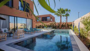 Ein moderner Poolbereich mit Liegestühlen, einem klaren Pool und einem Gebäude mit großen Fenstern und einem Balkon.