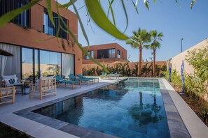 A modern pool area with lounge chairs, a clear pool, and a building with large windows and a balcony. - Villa Marleanis (Marrakech)