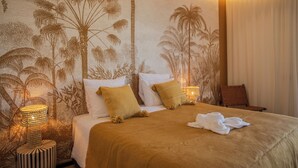 Une chambre d’hôtel avec un lit, des oreillers, une table de chevet et un mur orné d’une fresque représentant un palmier.