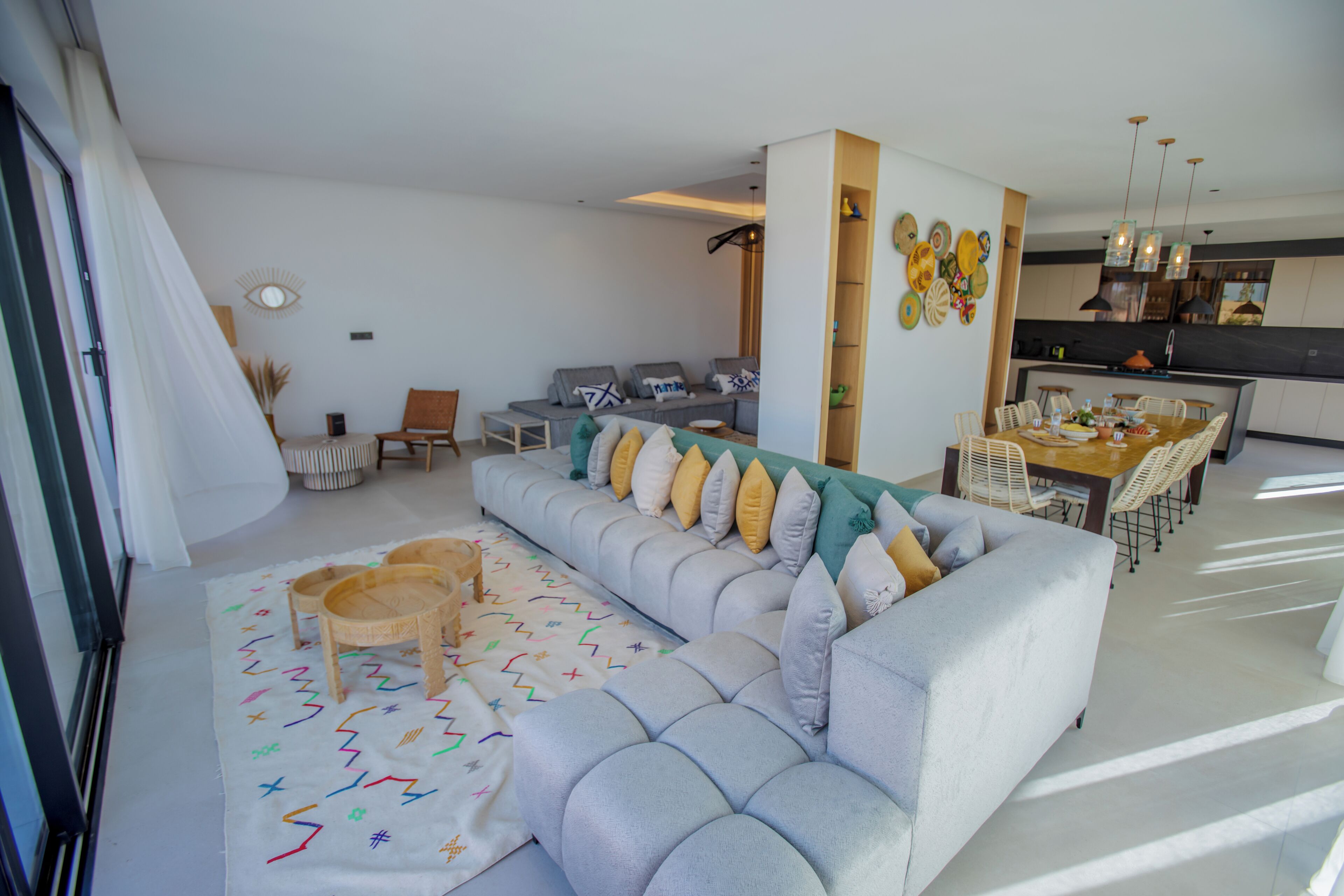 A modern living room with a grey sofa, a dining table, and a kitchen area.