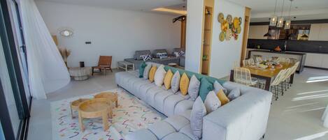 A modern living room with a grey sofa, a dining table, and a kitchen area.