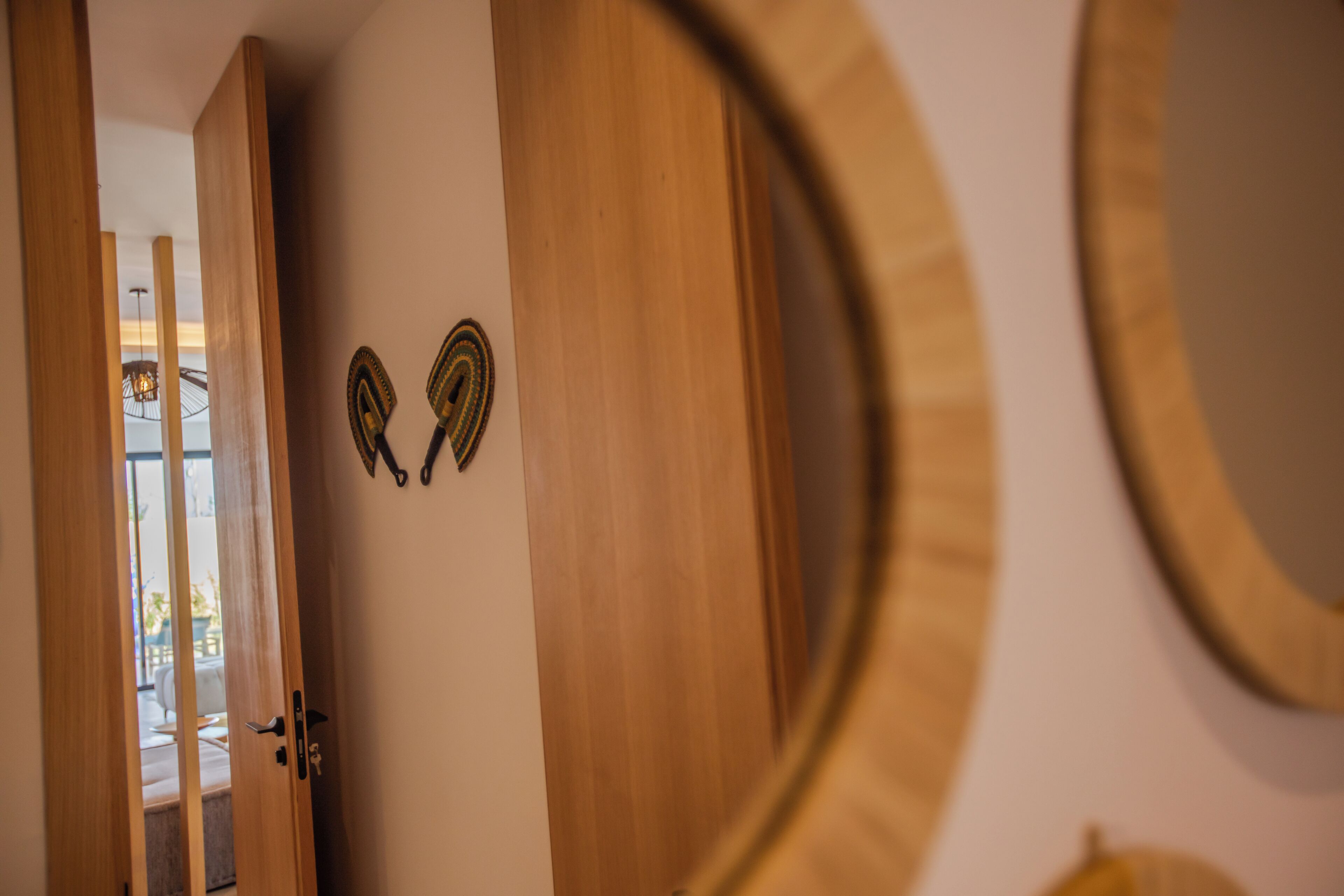 A wooden door with a keyhole and a small lock, a circular mirror on the wall, and a glimpse of a room with a chair and a table.