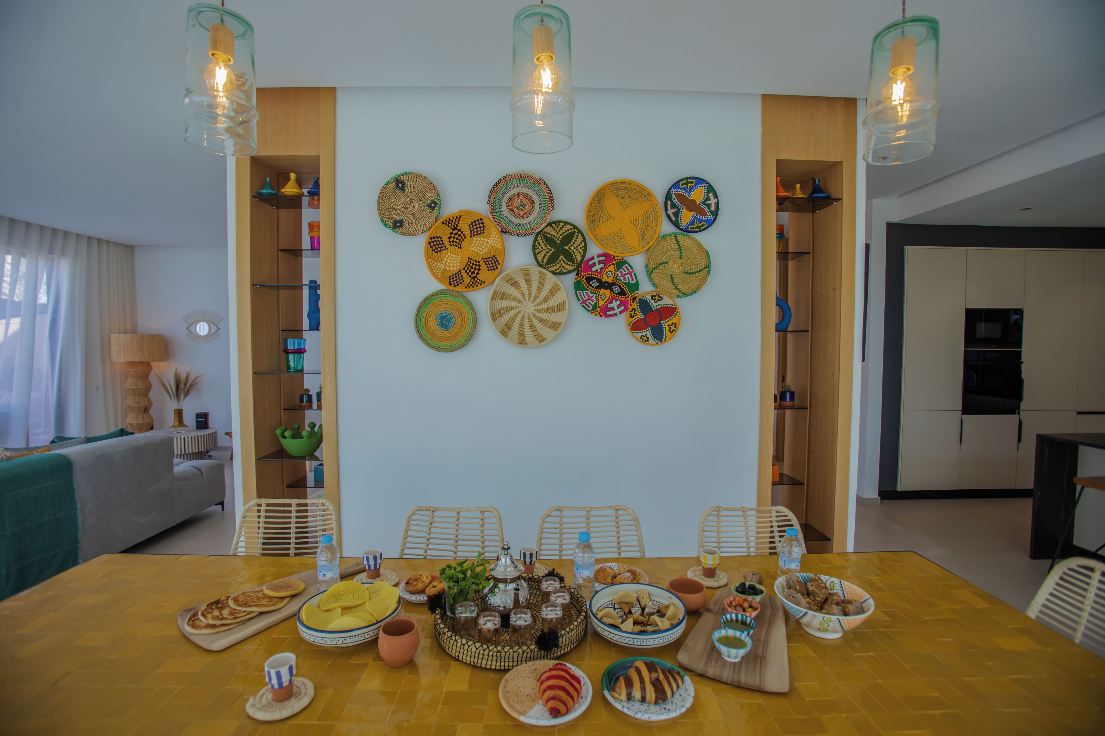 A dining area with a wooden table set for a meal, surrounded by chairs, and a wall decorated with woven plates.