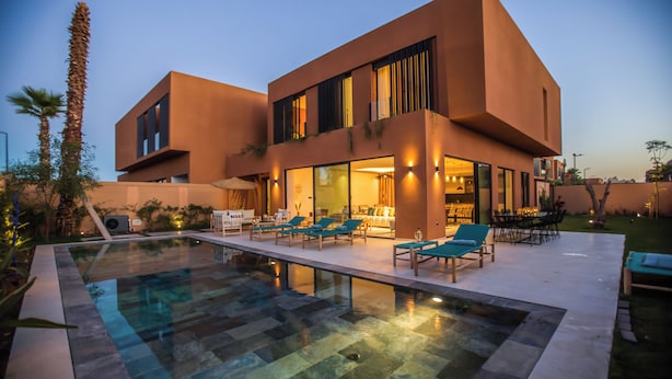 Une maison moderne à deux étages, dotée d’une piscine, d’un espace de détente extérieur et d’un jardin bien entretenu.