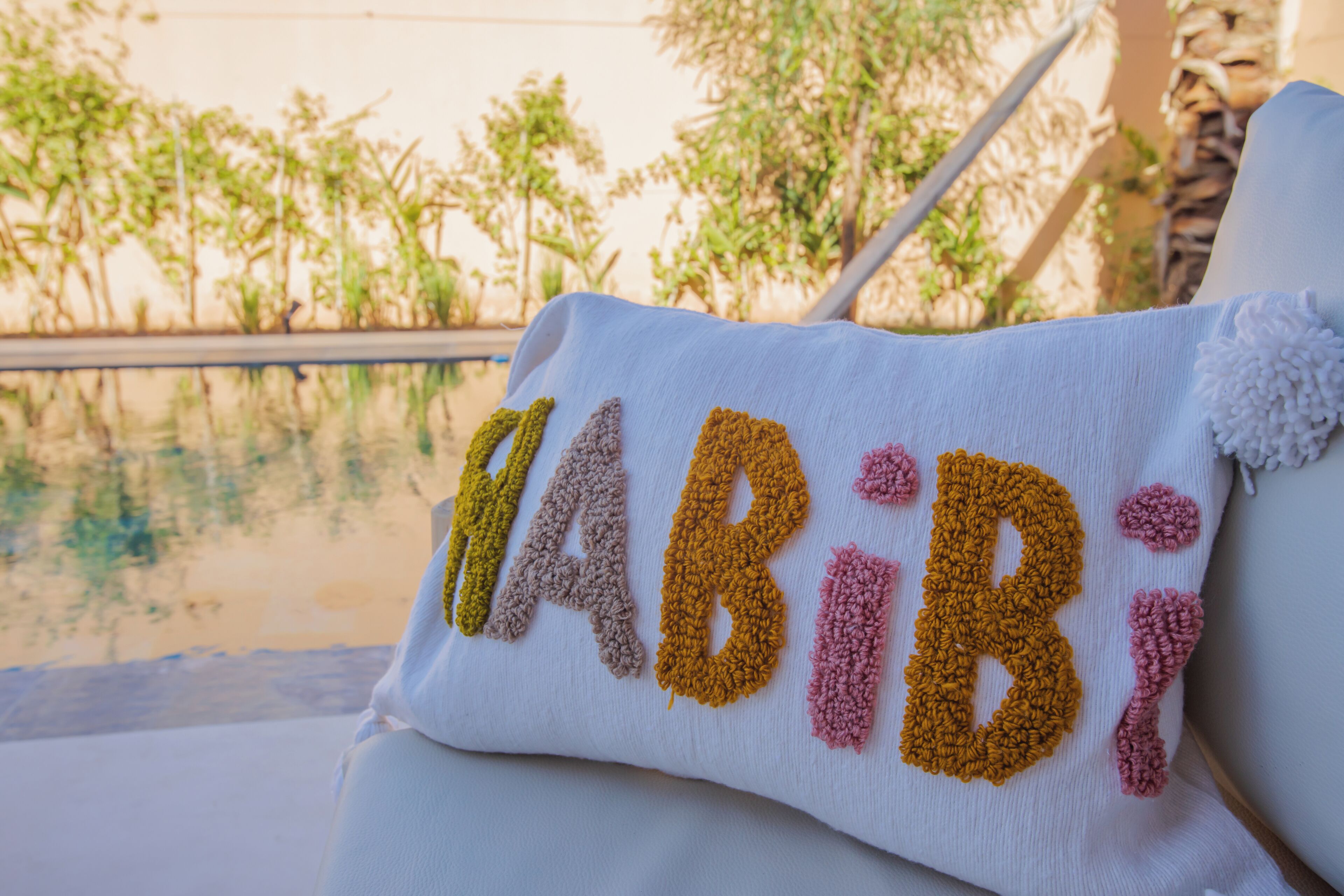 En vit kudde med ordet ”ABIBI” broderat i flerfärgat garn.