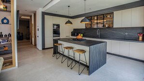 Une cuisine moderne dotée d’un îlot central, de tabourets de bar, de luminaires suspendus et d’un pare-feu en marbre.