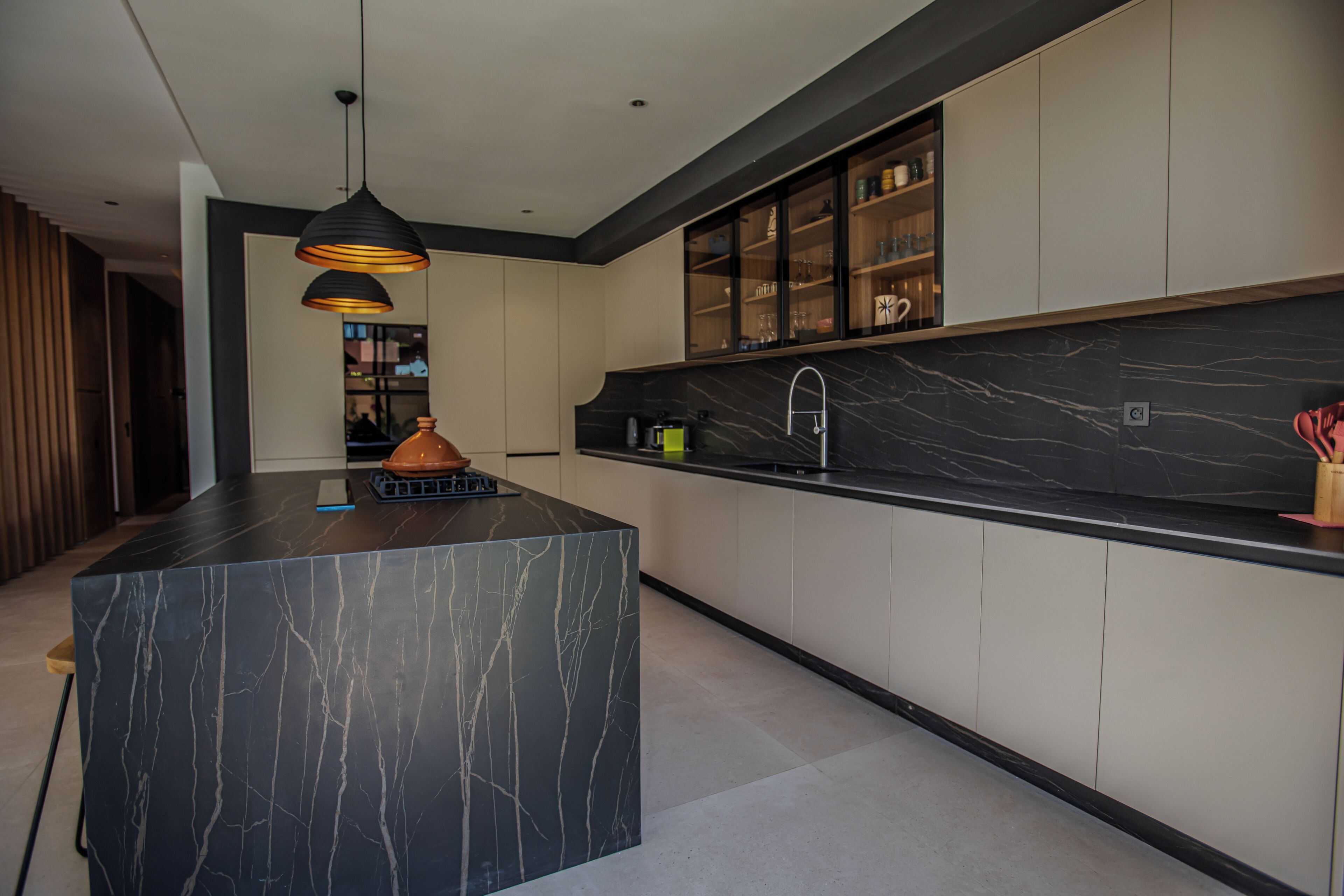 A modern kitchen with a marble island, pendant lighting, and built-in cabinets.