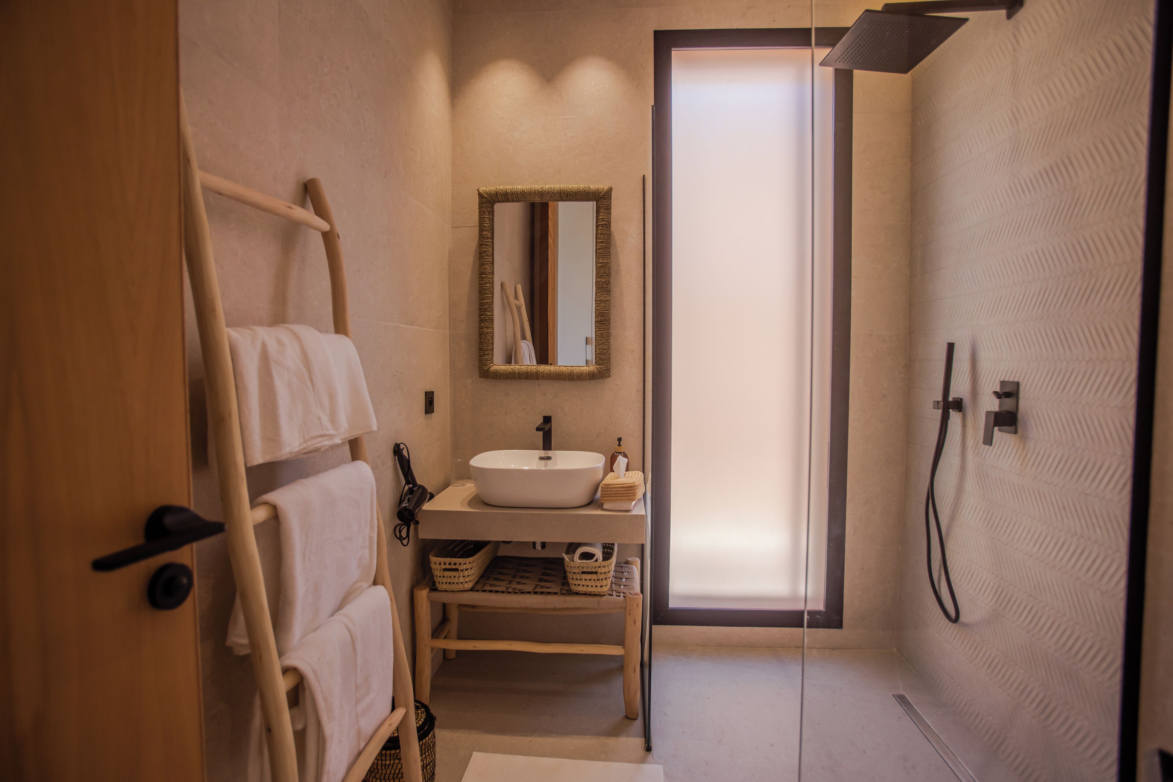 A modern bathroom with a wooden towel rack, a white sink, a mirror, and a shower area.