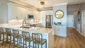 A modern kitchen with white cabinetry, stainless steel appliances, and a central island with bar stools. - Beautiful Waterfront, Pool, Private Hot Tub, Golf Cart, Kayaks, Bikes & Tennis (Alligator Point)