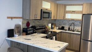Eine moderne Küche mit Holzschränken, einem Edelstahlkühlschrank, einer Mikrowelle und einer großen Kücheninsel mit Barhocker.