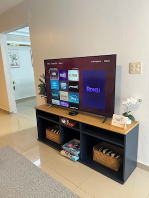 Televisor de pantalla plana sobre un soporte de madera mostrando una interfaz de Roku con varios servicios de transmisión.