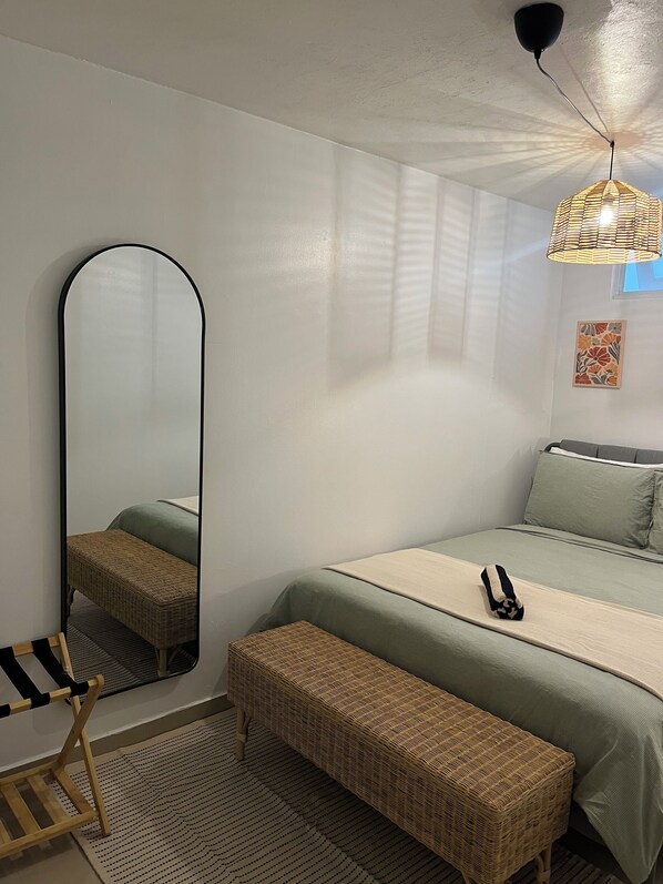 Un dormitorio con cama, un espejo grande, una lámpara colgante y un pequeño banco.