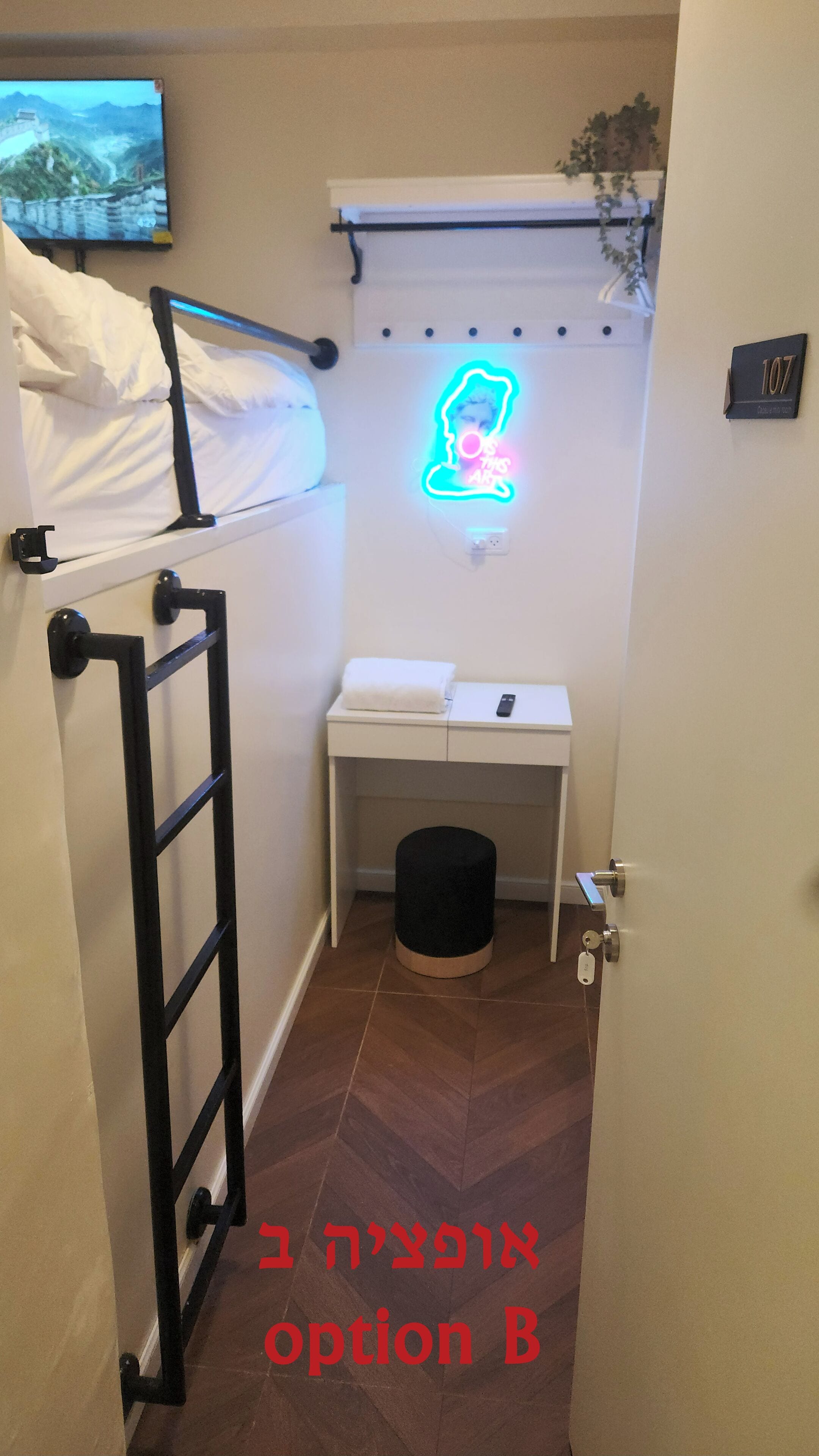 A small, narrow room with a bunk bed, a desk with a neon sign, a trash can, and a door with a lock.