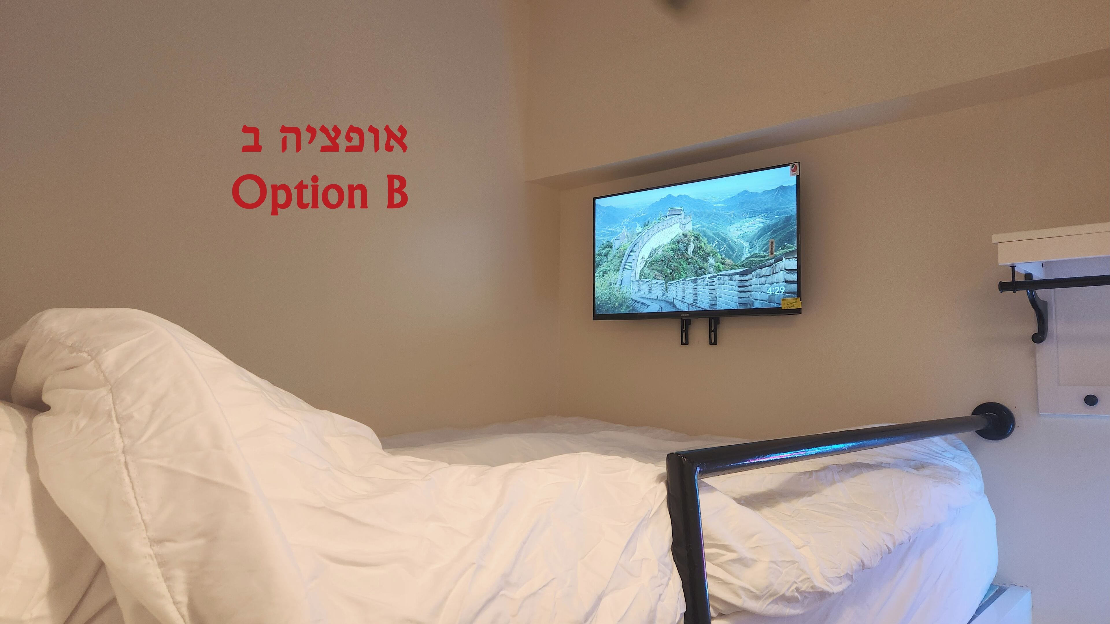 A bedroom with a bed, a mounted TV displaying a scenic landscape, and a wall-mounted shelf.