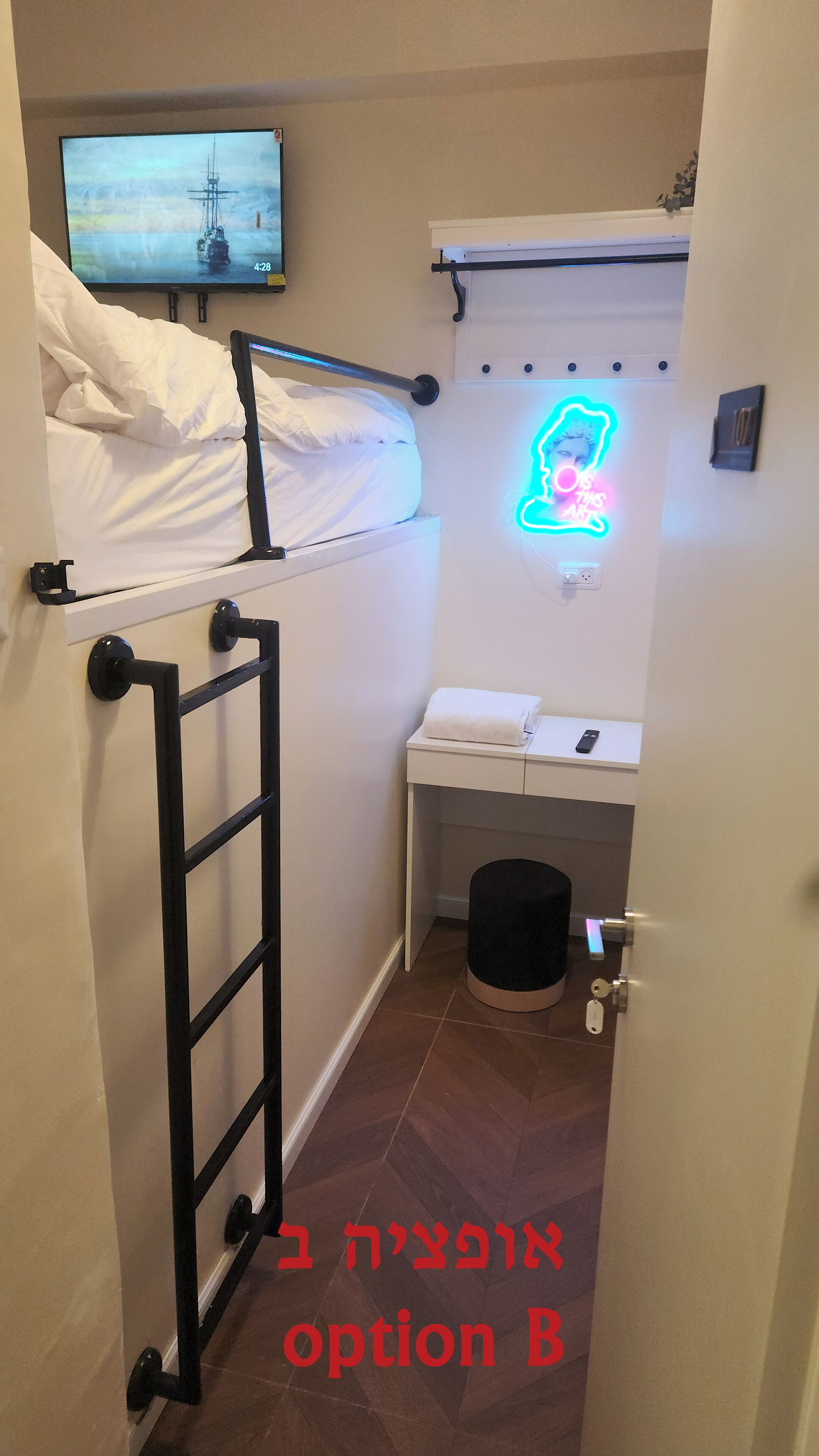 Una habitación pequeña y estrecha con una cama litera, un letrero de neón, una mesita con una toalla y una puerta con cerradura de llave.