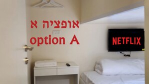 A small, compact room with a bed, a desk, and a TV mounted on the wall. - Jeru Caps CityCenter (Jerusalem)