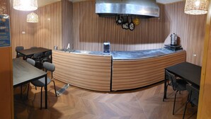 A shared dining area with a curved wooden counter, a stainless steel sink, and a modern light fixture. - Jeru Caps CityCenter (Jerusalem)