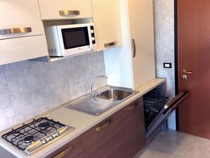 A compact kitchen with a gas stove, a microwave, a sink, and a dishwasher. - Modern Residence in the Heart of Bibione Spiaggia (San Michele al Tagliamento)