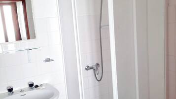Een badkamer met een wit wastafelmeubel, een spiegel en een douche met glazen wanden.