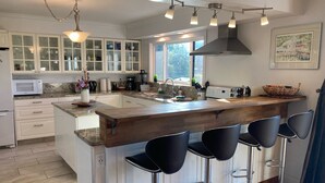 A modern kitchen with a large island, bar stools, and a window providing natural light. - AUTUMN SALE! Cedar Field House on 2 Acres - horseshoes, Volleyball, Fire pit (Eastsound)