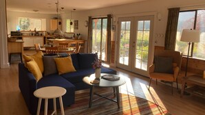 A spacious living area with a sofa, coffee table, and a view of the garden through large sliding doors. - AUTUMN SALE! Cedar Field House on 2 Acres - horseshoes, Volleyball, Fire pit (Eastsound)