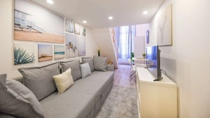 Ein modernes Wohnzimmer mit grauem Sofa, einem Flachbildfernseher auf einem weißen Schrank und Kunstwerken an den Wänden.