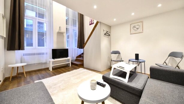 Ett modernt vardagsrum med en soffa, ett litet runt bord, en tv och en trappa som leder upp till en övre våning.