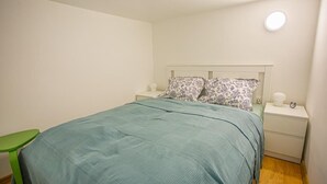 A bedroom with a bed, green chair, nightstands, and a bedside table with a lamp. - Boutique flat in Akacfa street (Budapest)