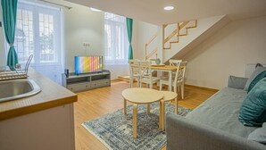 A modern apartment with a kitchen, dining area, and living room. It features a staircase, a colorful artwork on the wall, and a grey sofa. - Boutique flat in Akacfa street (Budapest)