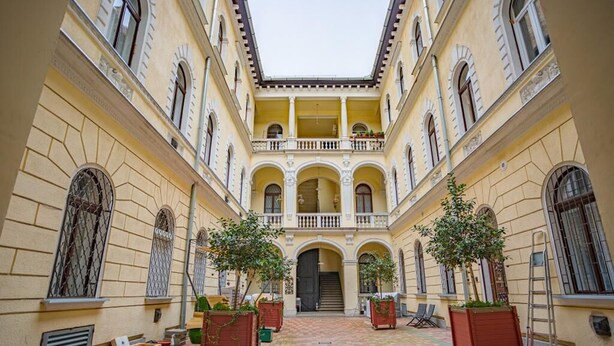 Un patio con una escalera central, plantas en macetas y vistas al interior del edificio.