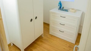 Una habitación con un armario blanco, un pequeño tocador blanco y una ventana decorada con un decorativo de tabla de surf azul.