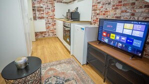 Una cocina compacta con salpicadero de ladrillo, horno empotrado, microondas y un televisor mostrando una interfaz de televisión en vivo.