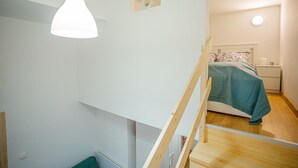 Un dormitorio con una cama litera, una escalera de madera, una mesita de noche y un buró.