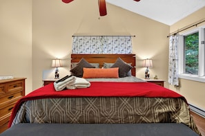 Ein Schlafzimmer mit einem Bett, Nachttischen, einem Fenster mit Vorhängen und einem Deckenventilator.