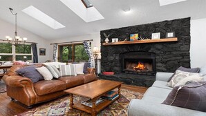 Een woonkamer met een stenen openhaard, een leren bank en een eethoek met een tafel en stoelen.
