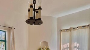 Una zona de menjador amb una taula preparada per a quatre, un lampadari, un ram de flors i una finestra amb cortines.