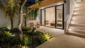 Ein modernes Haus mit Glastür, die zu einem Schlafzimmer, einer Treppe und einem Garten mit tropischen Pflanzen führt.