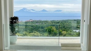 Ein Balkon mit Glasgeländer, einem Blumentopf und Blick auf eine Berglandschaft sowie das Meer.