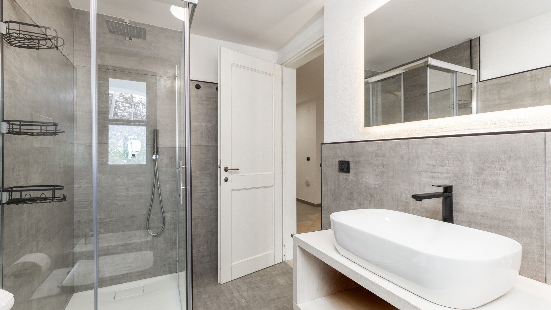 A modern bathroom with a glass-enclosed shower, a white sink, and a large mirror above the sink.