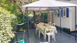 Un patio coperto con tavolo e sedie, immerso nel verde e adiacente a una casa.