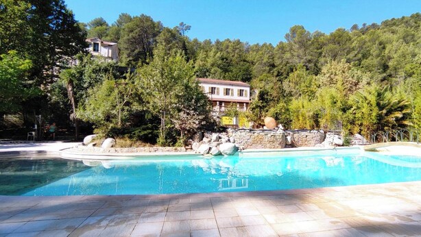 Una piscina con bordo in pietra, circondata da alberi e da un muro in pietra.