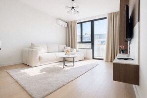 A modern living room with a sofa, a coffee table, a TV mounted on the wall, and a large window with curtains. - Boutique Hotel Echo Residence (Belgrade)