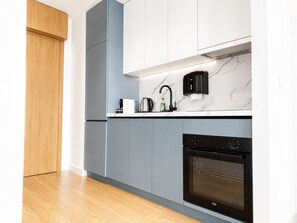 Une cuisine moderne avec des meubles gris, un four noir et un pare-feu en marbre.