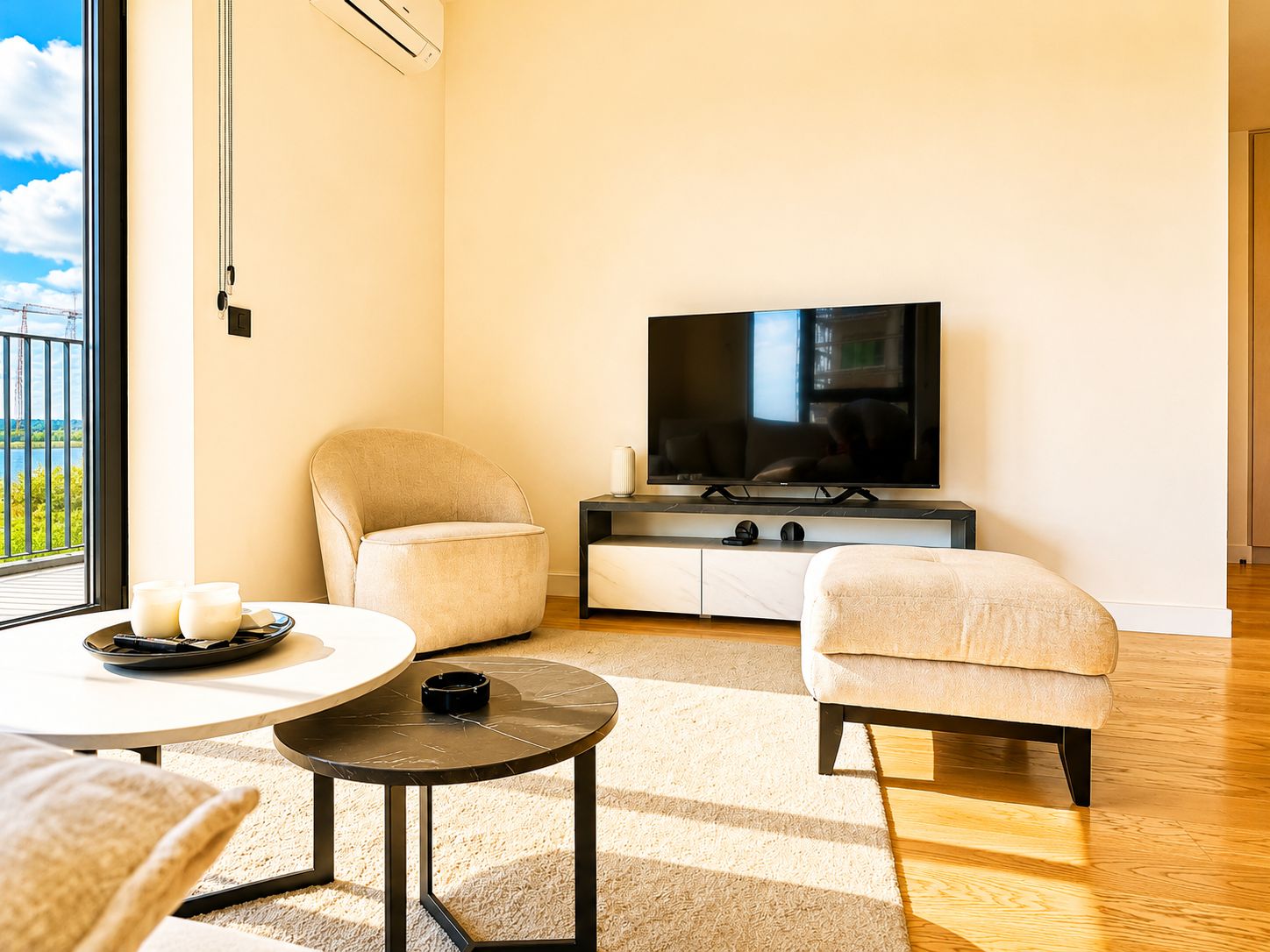 Una sala de estar moderna con un televisor de pantalla plana, dos sillones, una mesa de centro y vistas al exterior.